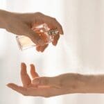 Person applying perfume spray onto their wrist with a fragrance bottle.