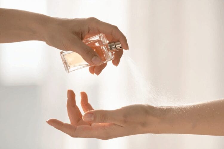 Person applying perfume spray onto their wrist with a fragrance bottle.
