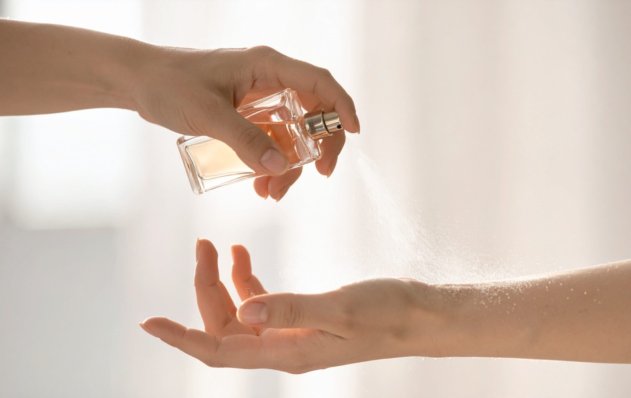Person applying perfume spray onto their wrist with a fragrance bottle.