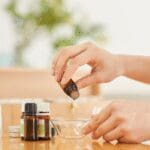 Person preparing a cosmetic formulation using essential oils and ingredients in a cosmetic laboratory.