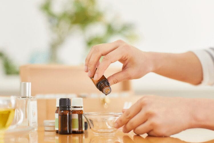 Person preparing a cosmetic formulation using essential oils and ingredients in a cosmetic laboratory.