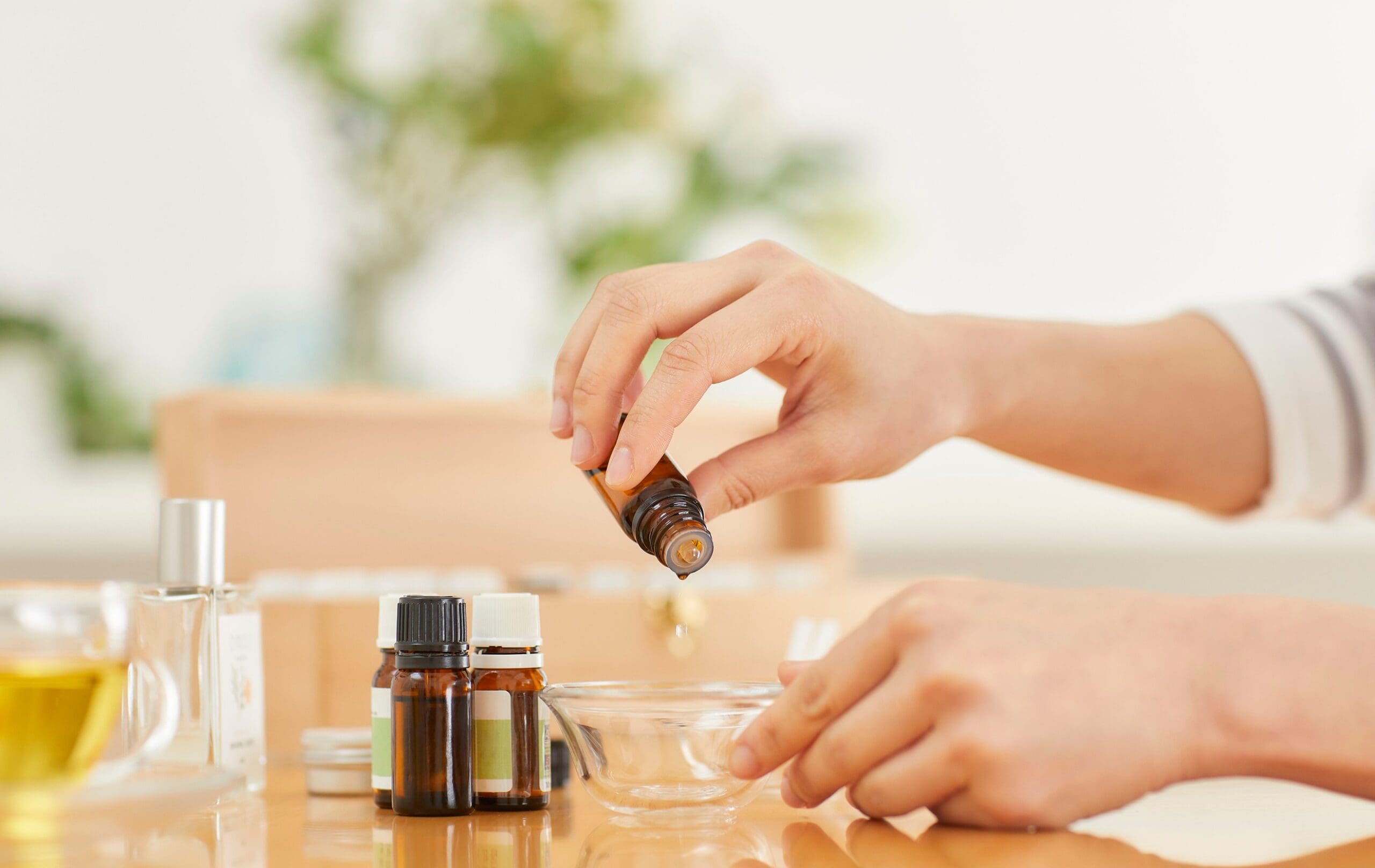 Person preparing a cosmetic formulation using essential oils and ingredients in a cosmetic laboratory.