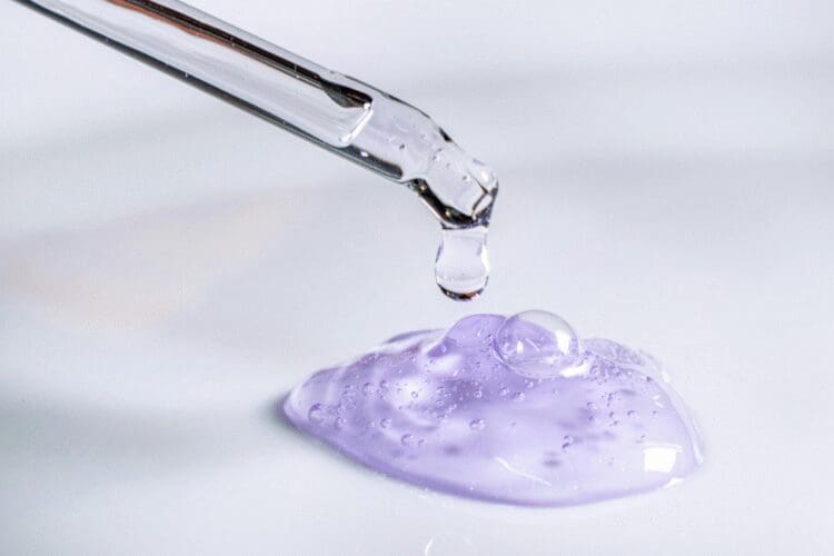 Close-up of a cosmetic serum being dispensed from a dropper onto a gel formulation.