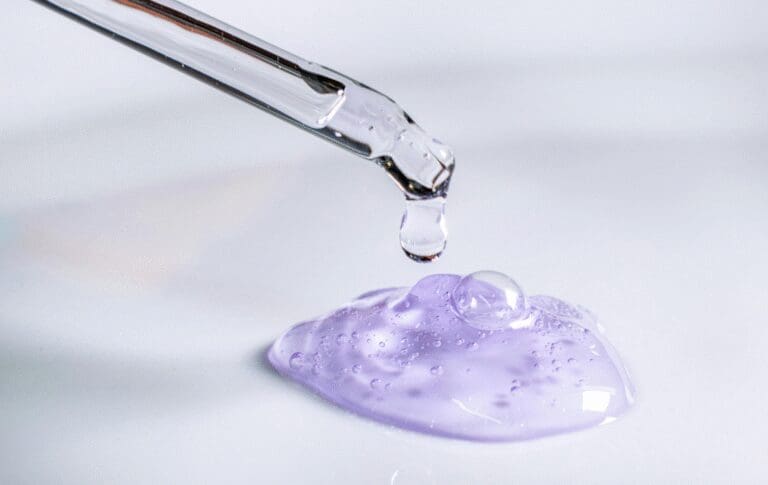 Close-up of a cosmetic serum being dispensed from a dropper onto a gel formulation.