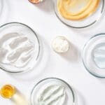 Various cosmetic formulations including creams, gels, oils and skincare ingredients displayed in laboratory dishes.