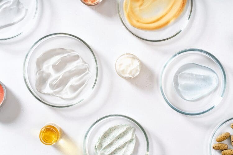 Various cosmetic formulations including creams, gels, oils and skincare ingredients displayed in laboratory dishes.