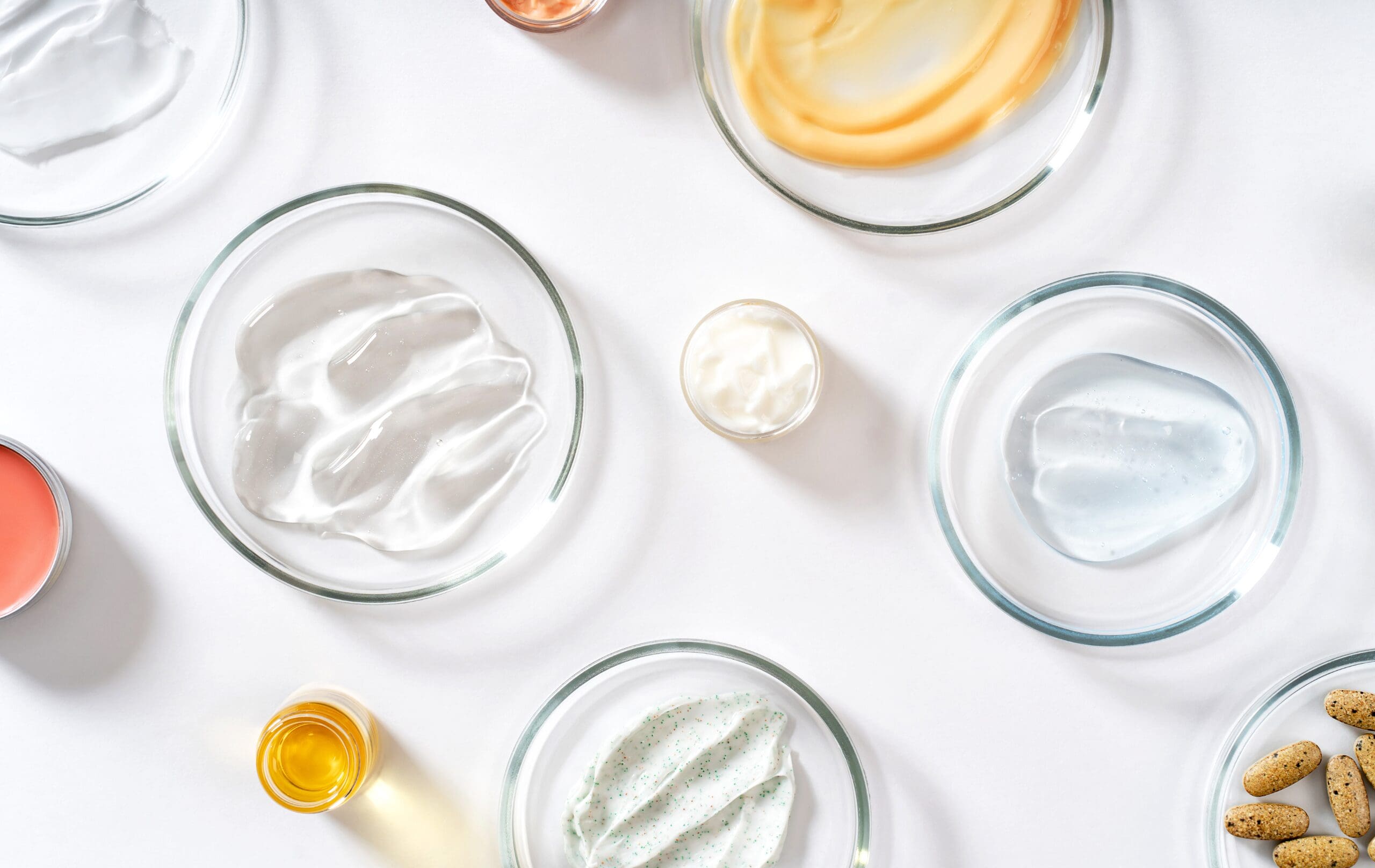 Various cosmetic formulations including creams, gels, oils and skincare ingredients displayed in laboratory dishes.