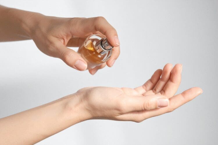 Hands applying a cosmetic serum or skincare product from a glass bottle onto the palm.