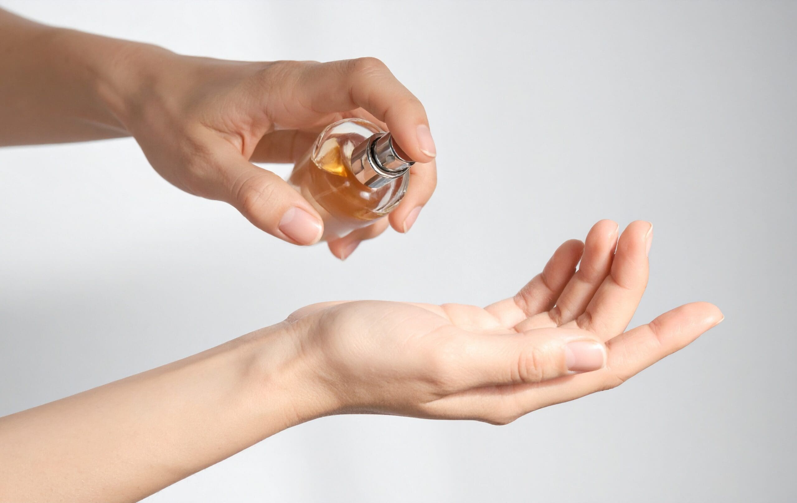 Hands applying a cosmetic serum or skincare product from a glass bottle onto the palm.
