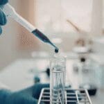 Laboratory technician transferring liquid sample into a test tube using a pipette.