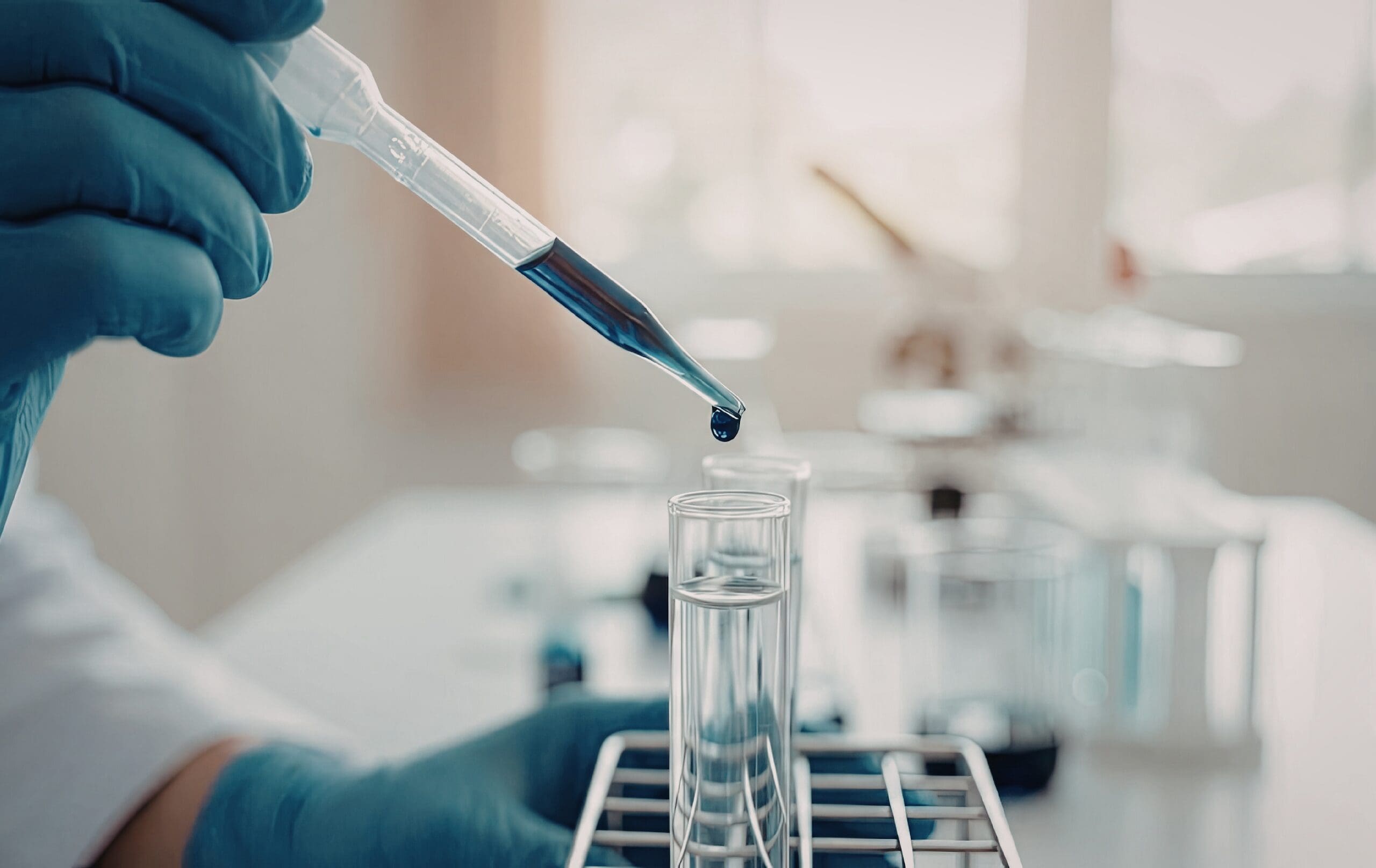 Laboratory technician transferring liquid sample into a test tube using a pipette.