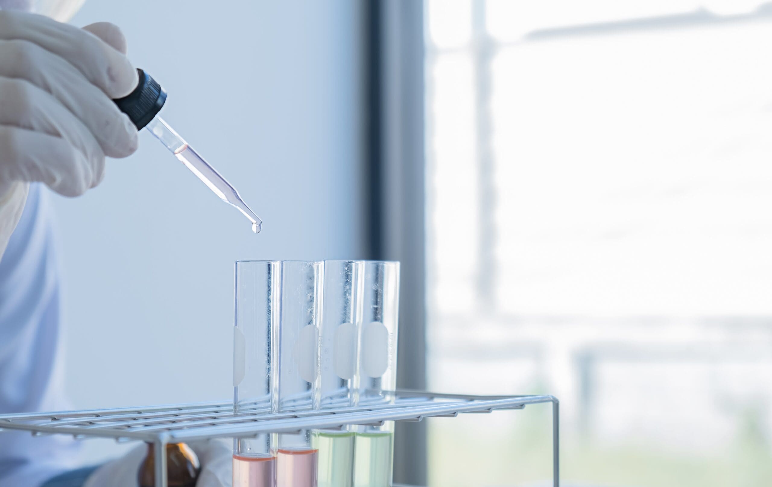 Laboratory technician using a pipette to test samples in test tubes.