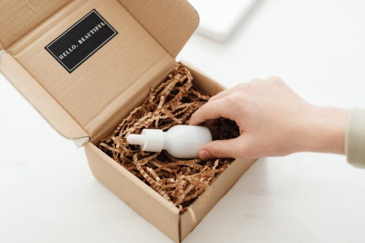 Hand placing a cosmetic serum bottle into eco-friendly packaging for cosmetic product distribution.