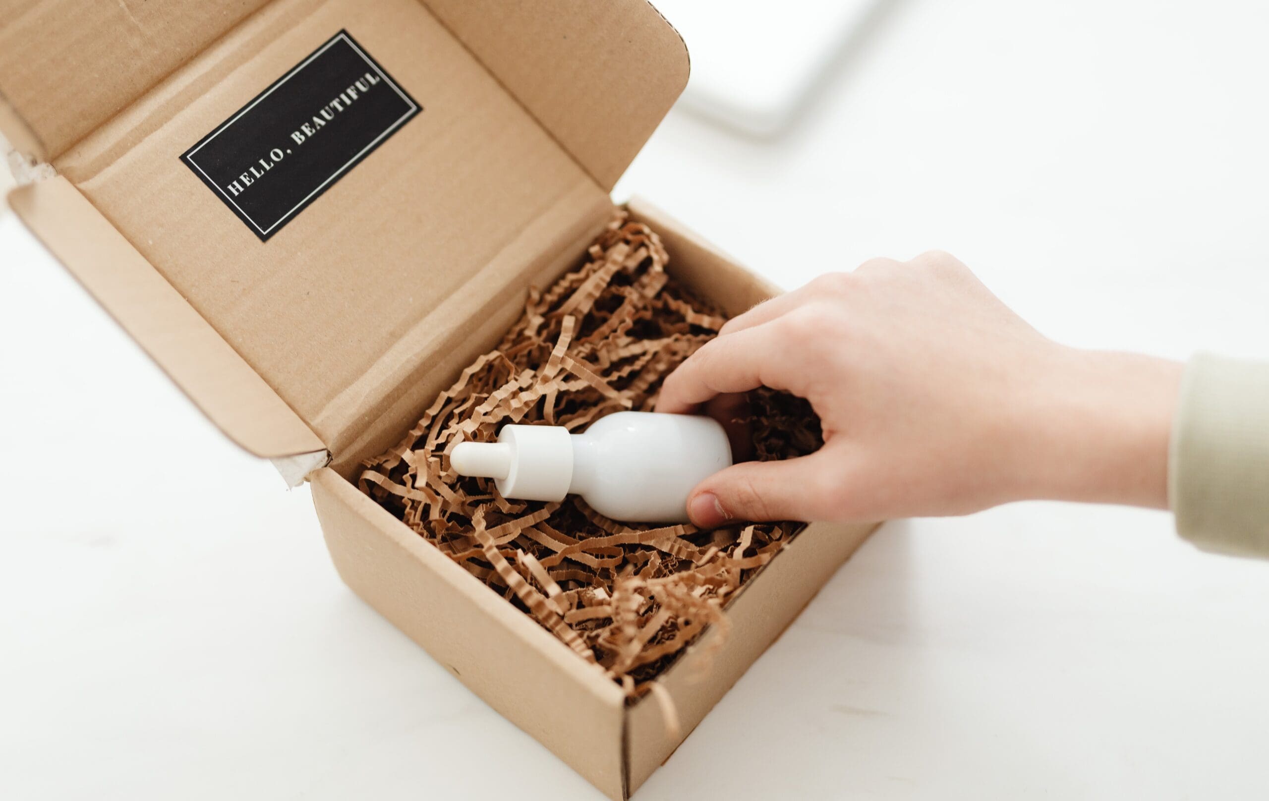 Hand placing a cosmetic serum bottle into eco-friendly packaging for cosmetic product distribution.