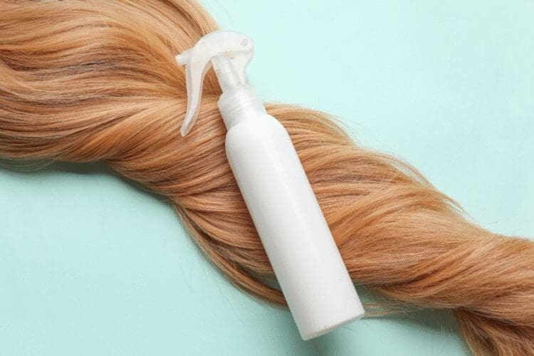Hair care spray bottle placed on blonde hair, representing cosmetic hair care products.