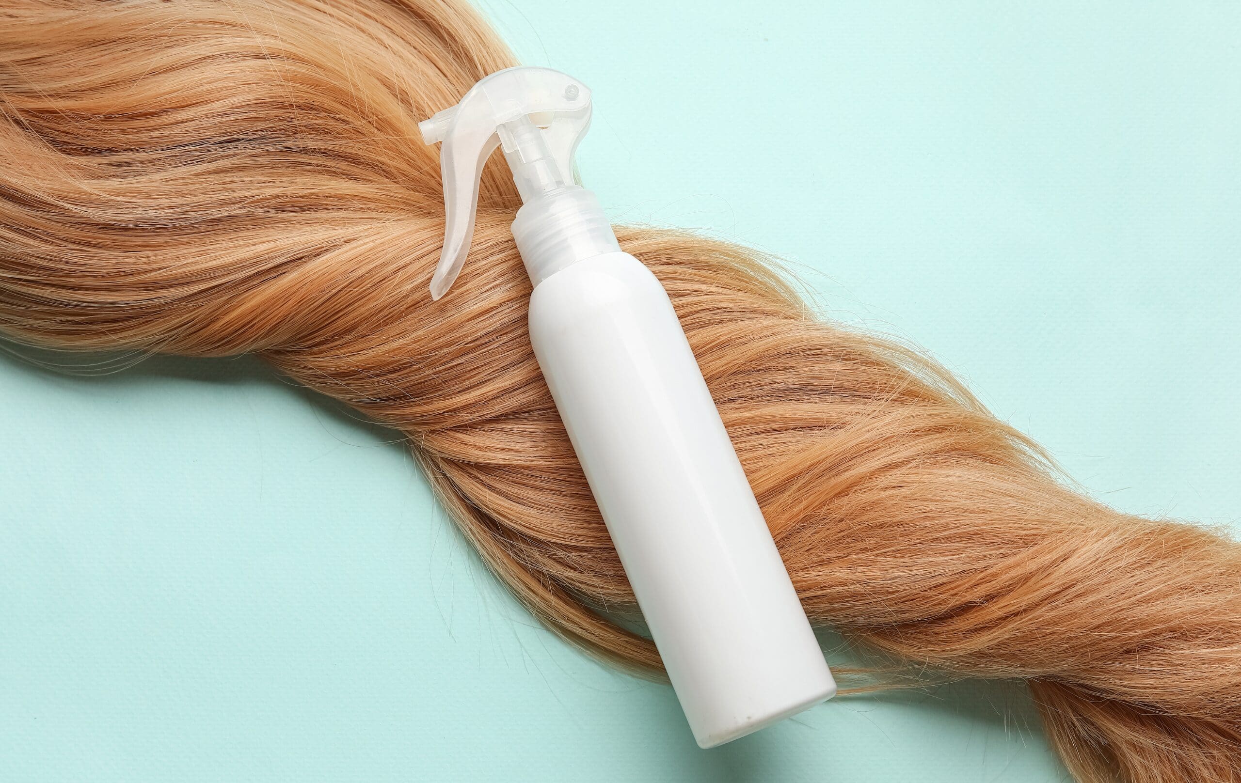 Hair care spray bottle placed on blonde hair, representing cosmetic hair care products.