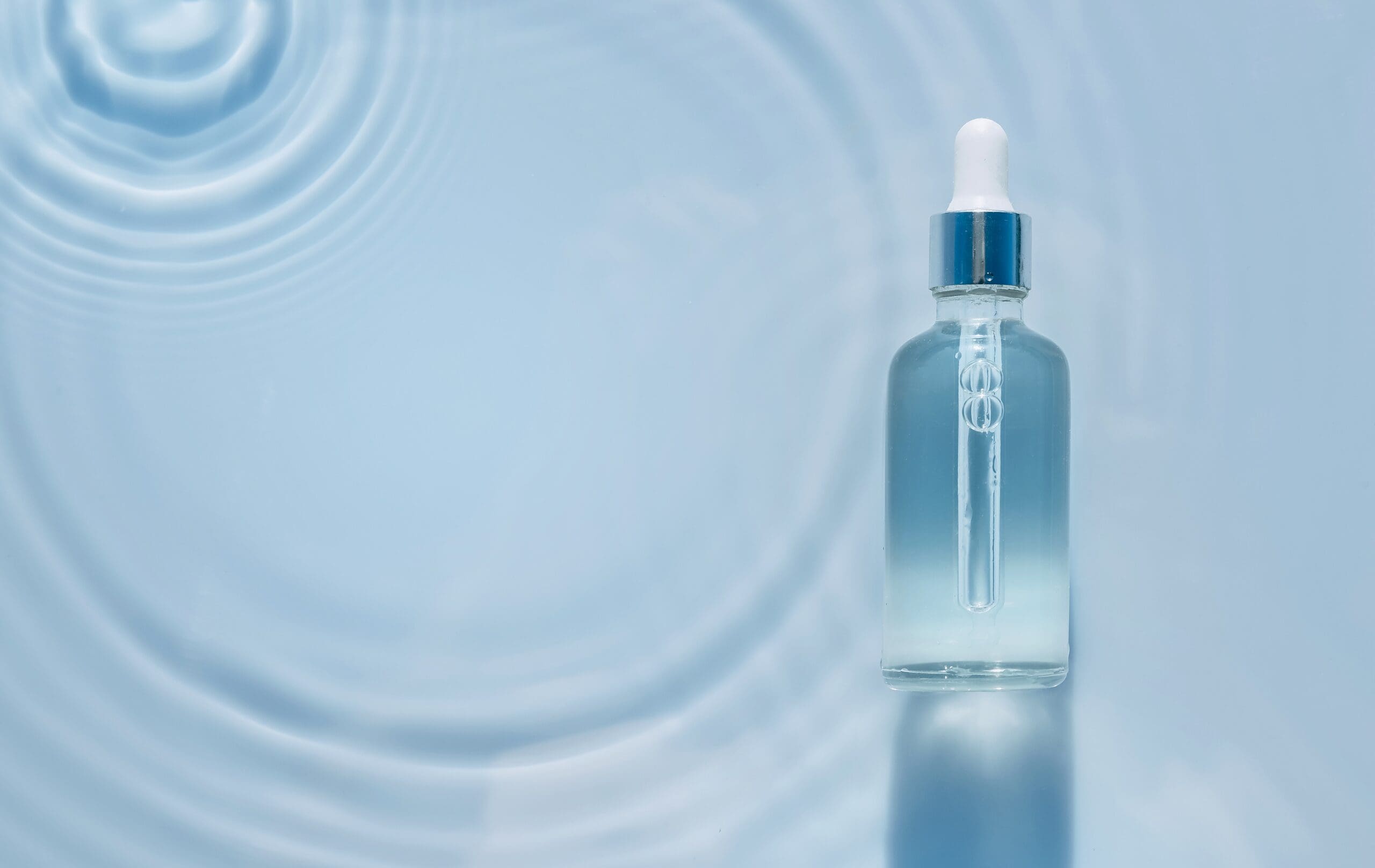 Hydrating facial serum in a dropper bottle displayed on a blue background with water ripples.