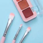 Eyeshadow palette with cosmetic makeup brushes on a pastel blue background.