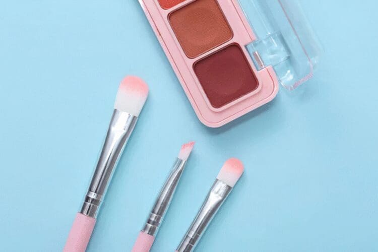 Eyeshadow palette with cosmetic makeup brushes on a pastel blue background.