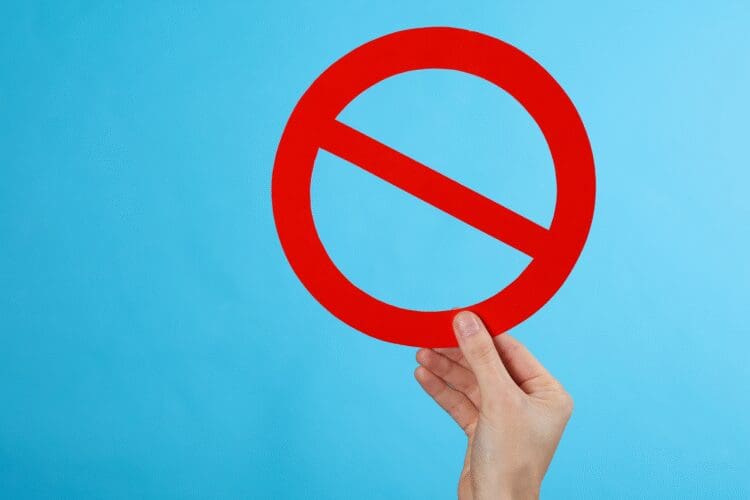 Hand holding a prohibition sign representing restricted substances and regulatory compliance requirements.