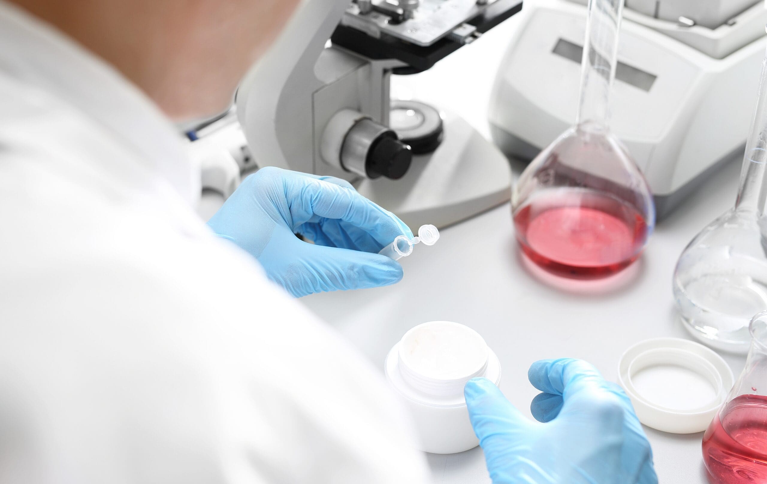 Scientist performing laboratory testing on a cosmetic cream formulation using scientific equipment.