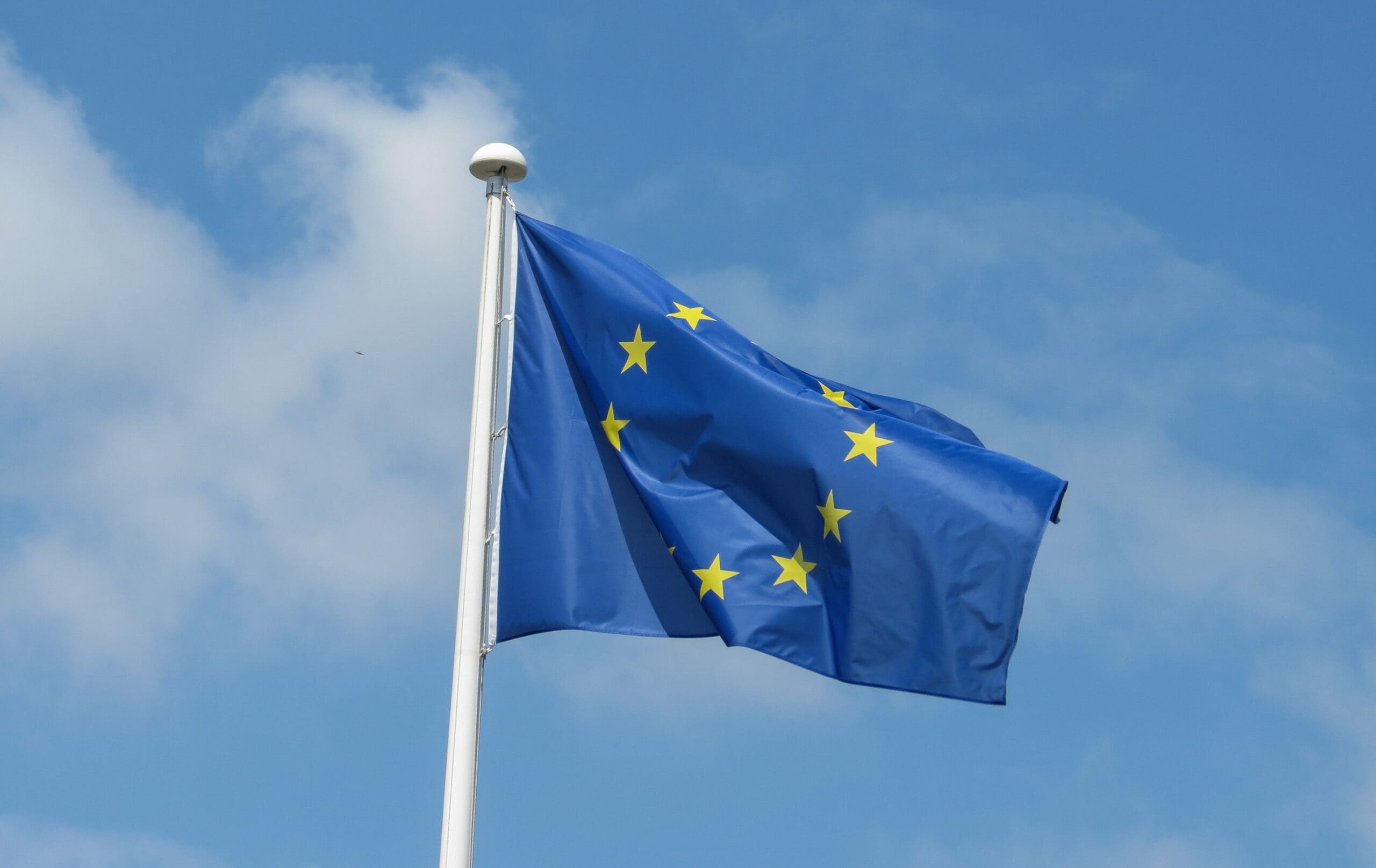 European Union flag waving against a cloudy blue sky representing EU regulations and compliance.