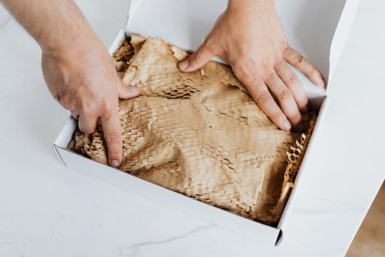Person packing a cardboard box with recyclable paper filling, representing sustainable packaging and packaging compliance.