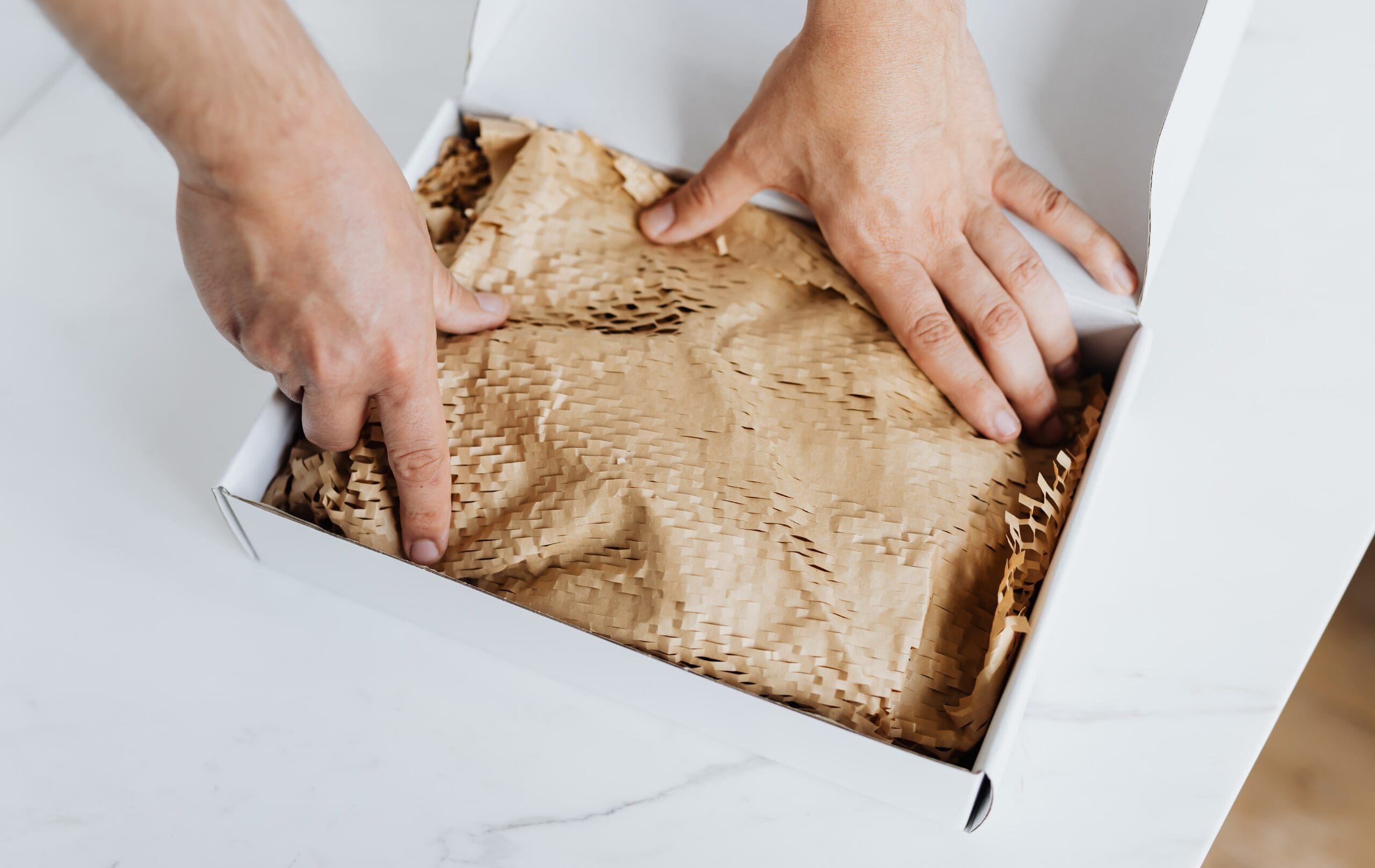 Person packing a cardboard box with recyclable paper filling, representing sustainable packaging and packaging compliance.