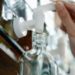 Person refilling a glass cosmetic bottle from a dispenser, representing reusable packaging and sustainable cosmetics.