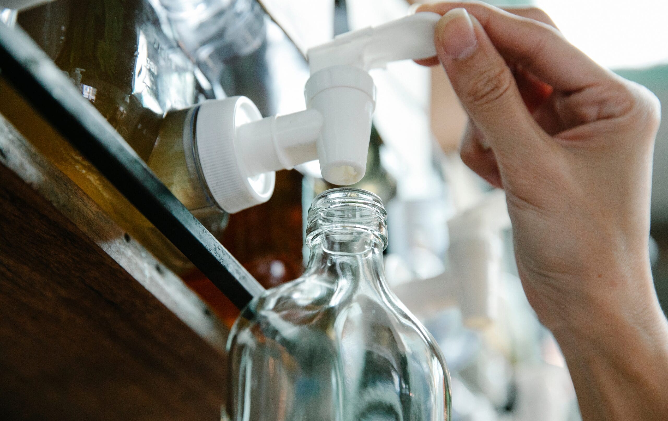Person refilling a glass cosmetic bottle from a dispenser, representing reusable packaging and sustainable cosmetics.