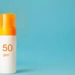 SPF 50 sunscreen cosmetic product in a pump bottle on a blue background.