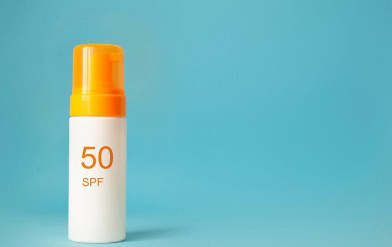 SPF 50 sunscreen cosmetic product in a pump bottle on a blue background.