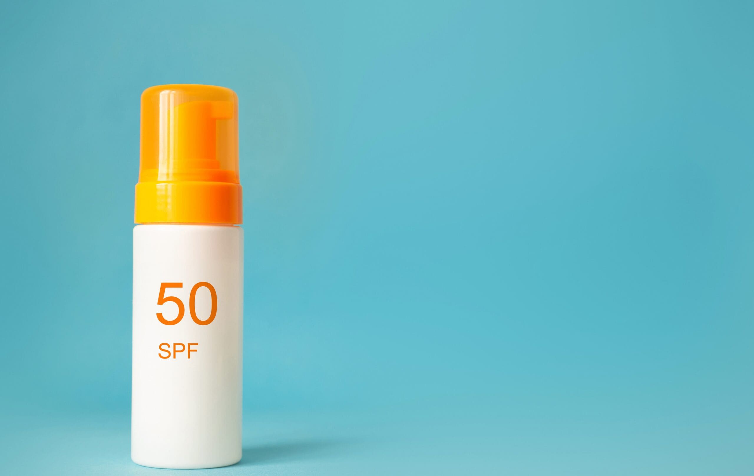 SPF 50 sunscreen cosmetic product in a pump bottle on a blue background.