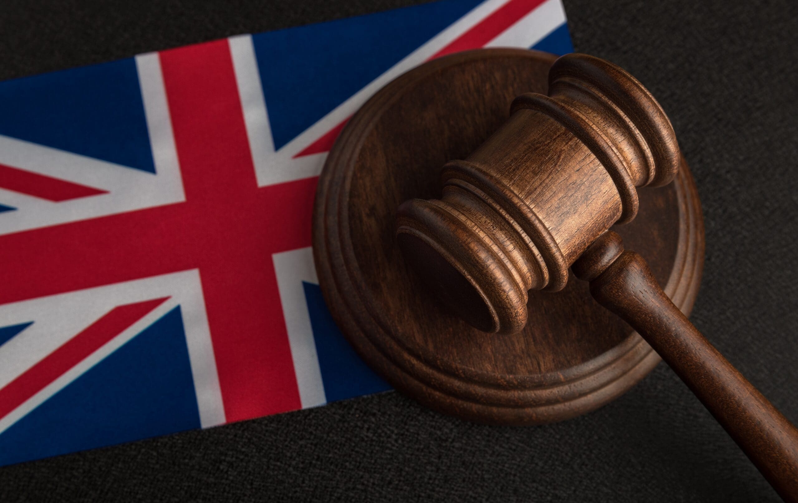 Wooden judge's gavel placed on a United Kingdom flag, representing UK regulations, legislation, and legal compliance.