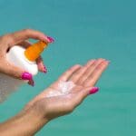 Person applying sunscreen lotion from a pump bottle onto their hand.