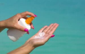 Person applying sunscreen lotion from a pump bottle onto their hand.