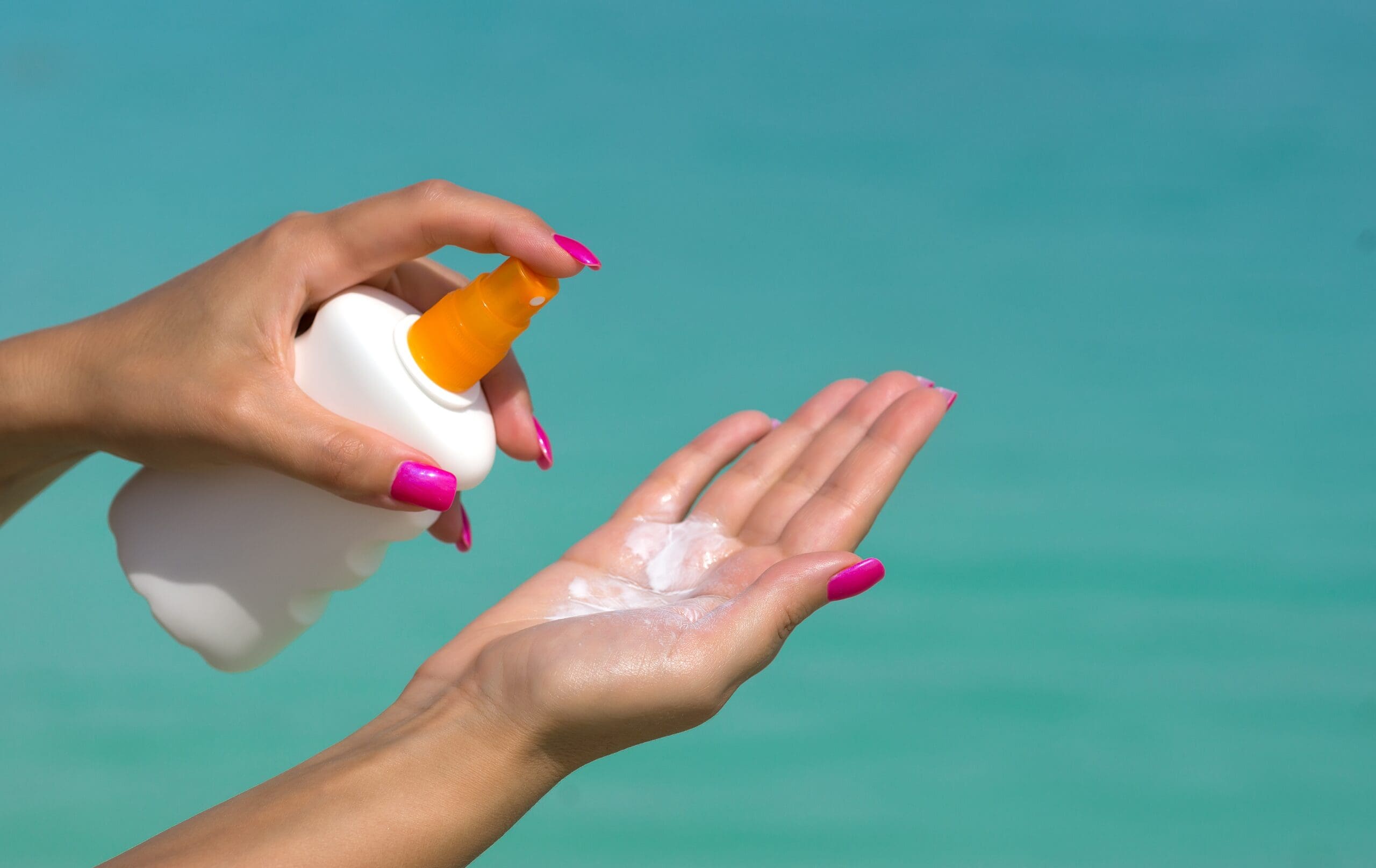 Person applying sunscreen lotion from a pump bottle onto their hand.