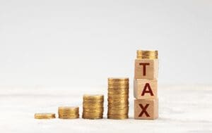 Stacks of coins beside wooden blocks spelling tax, representing taxation and financial obligations.