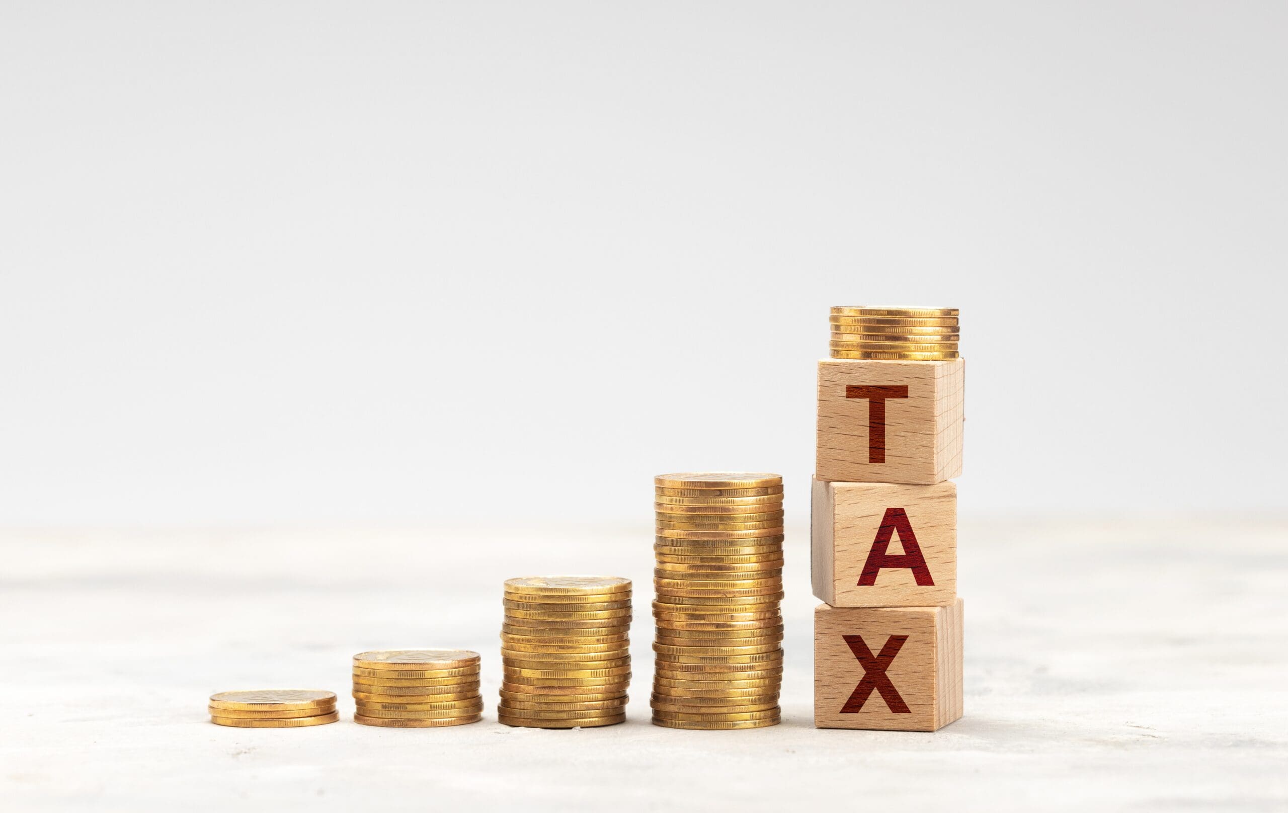 Stacks of coins beside wooden blocks spelling tax, representing taxation and financial obligations.
